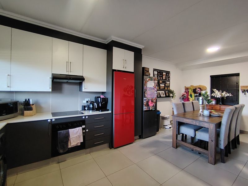 Open-plan kitchen and dining area featuring modern two-tone cabinetry, integrated appliances, and neutral tiled flooring throughout the space.