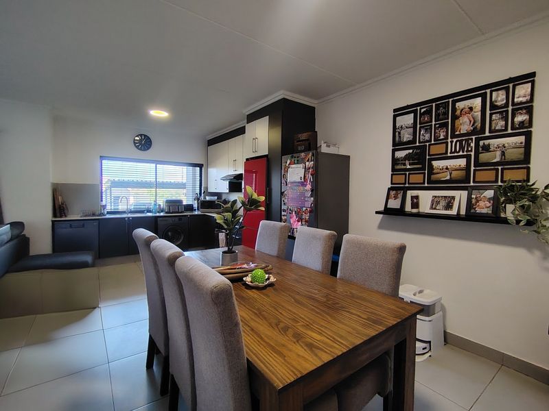 An open-plan living and dining area featuring a modern kitchen with dark cabinetry, tiled floors, and integrated appliances.