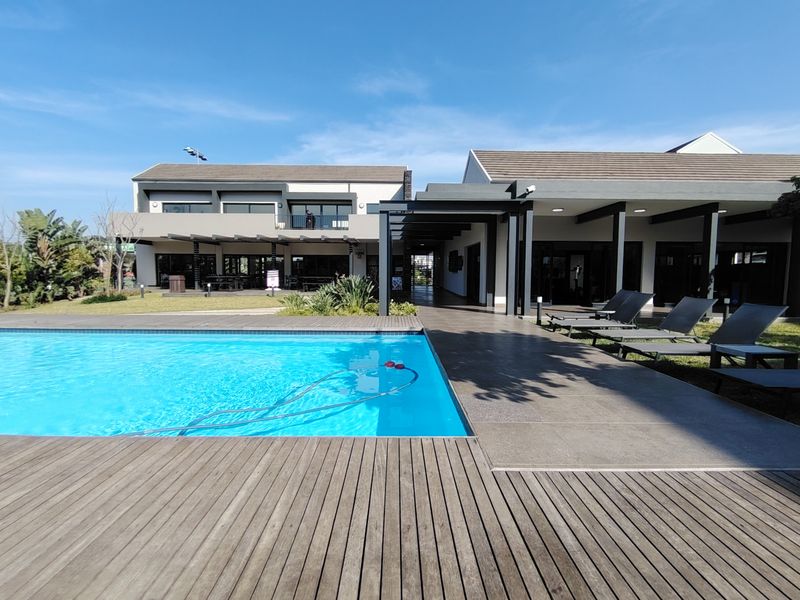 A well-maintained communal pool area featuring timber decking, a tiled patio, and a covered walkway connecting the building structures.