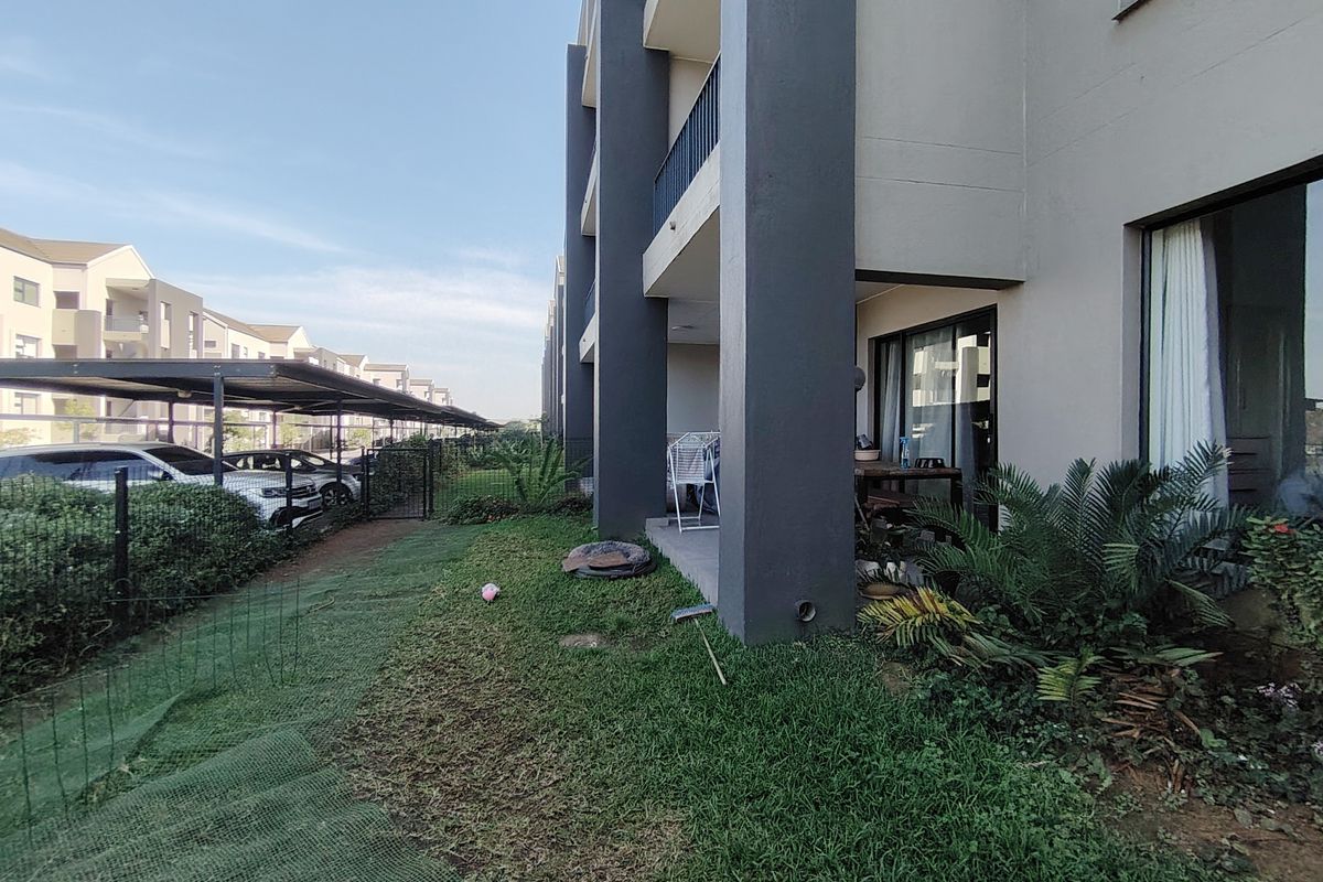 Ground floor apartment exterior featuring a covered patio, sliding glass doors, and a small private garden area.