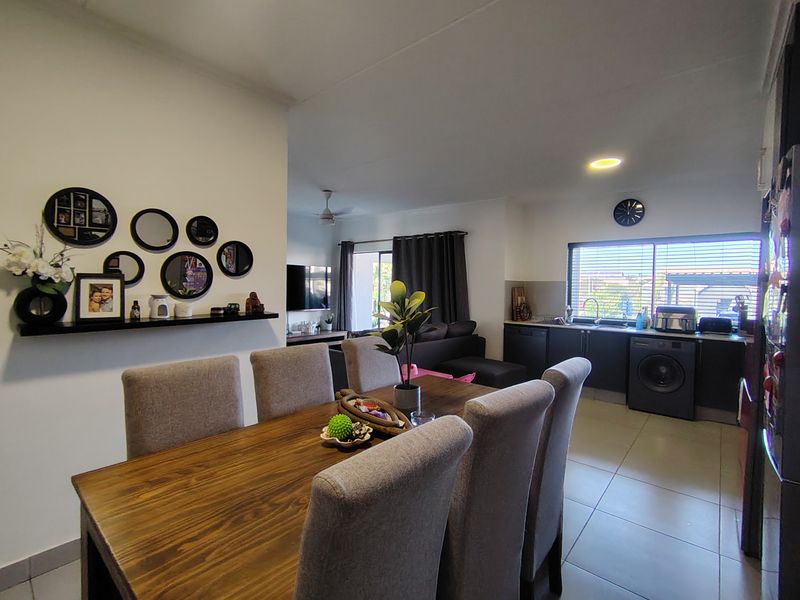 An open-plan living and dining area featuring tiled floors, a functional kitchen with built-in cabinetry, and integrated laundry appliances.