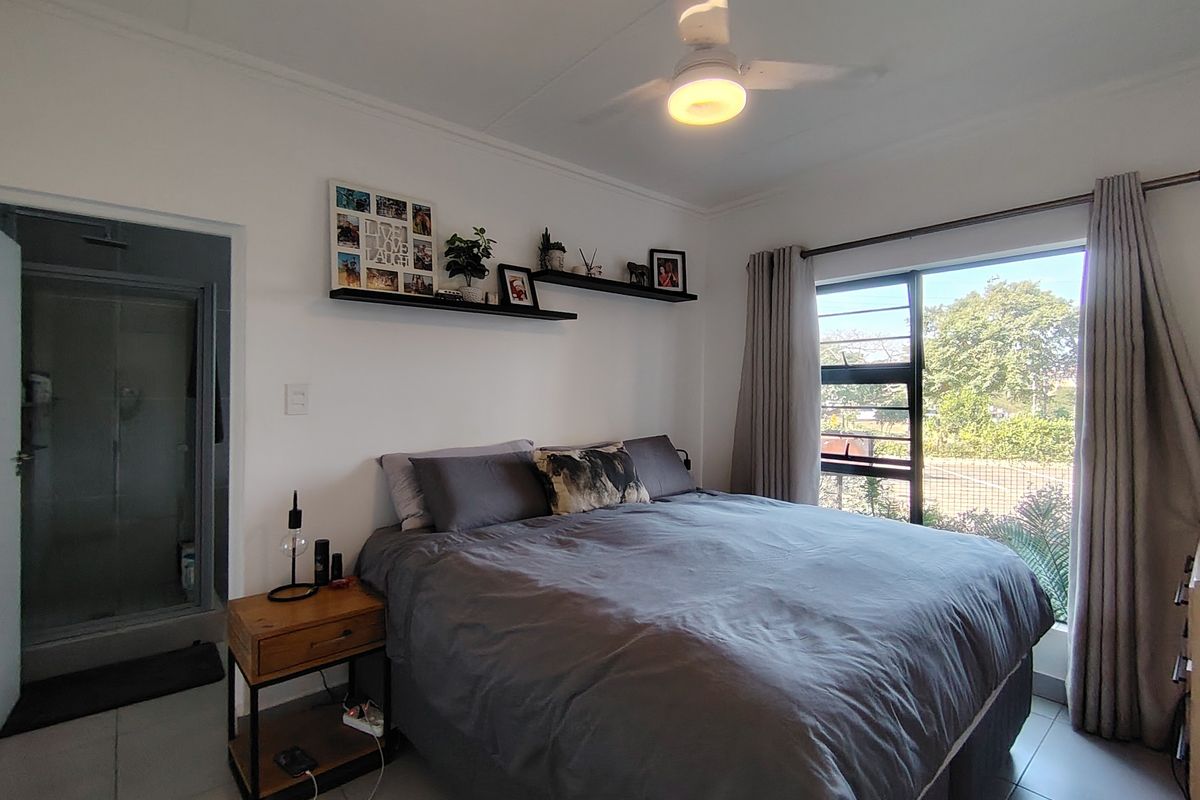 A well-maintained bedroom featuring tiled flooring, a ceiling fan, and an integrated en-suite bathroom with a shower.