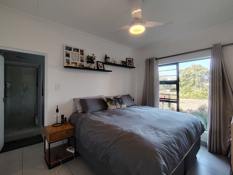 A well-maintained bedroom featuring tiled flooring, a ceiling fan, and an integrated en-suite bathroom with a shower.