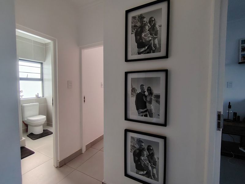 A clean and well-maintained hallway featuring neutral tiled flooring and access to adjacent rooms, including a bathroom.