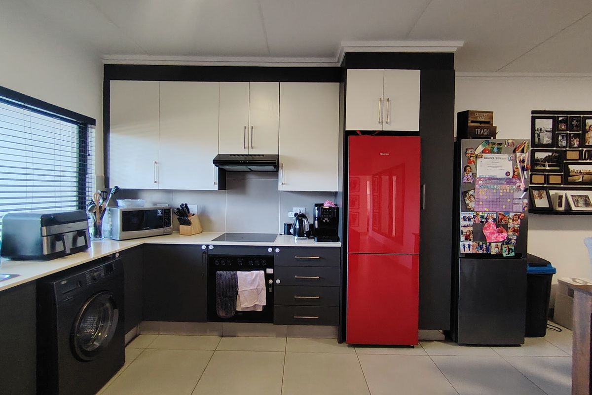 A modern kitchen featuring two-tone cabinetry, integrated appliances, an electric hob, and tiled flooring, offering a functional and contemporary cooking space.