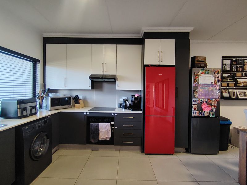 A modern kitchen featuring two-tone cabinetry, integrated appliances, an electric hob, and tiled flooring, offering a functional and contemporary cooking space.