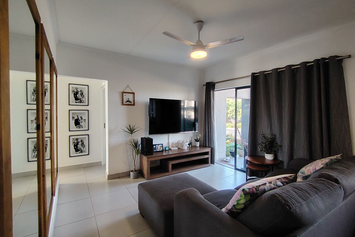 A well-maintained living room featuring tiled flooring, a ceiling fan, and a sliding glass door providing access to the outdoor area.