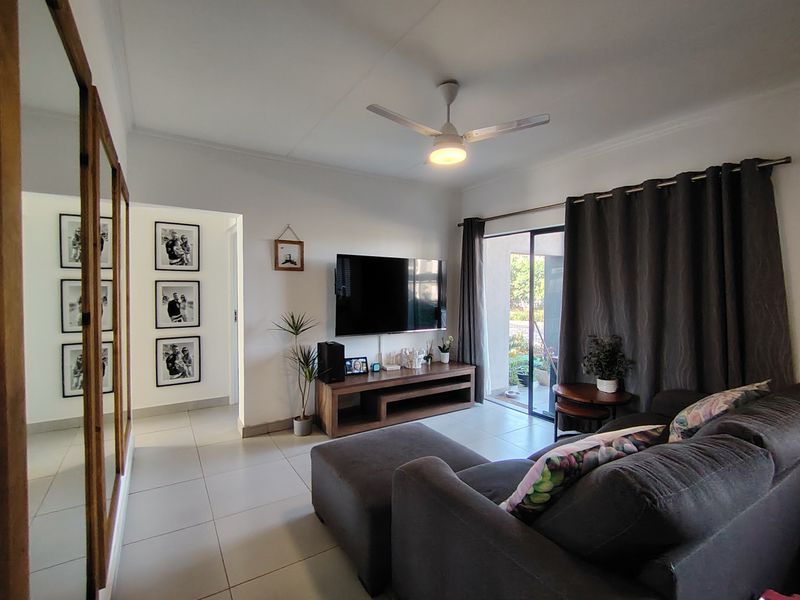 A well-maintained living room featuring tiled flooring, a ceiling fan, and a sliding glass door providing access to the outdoor area.