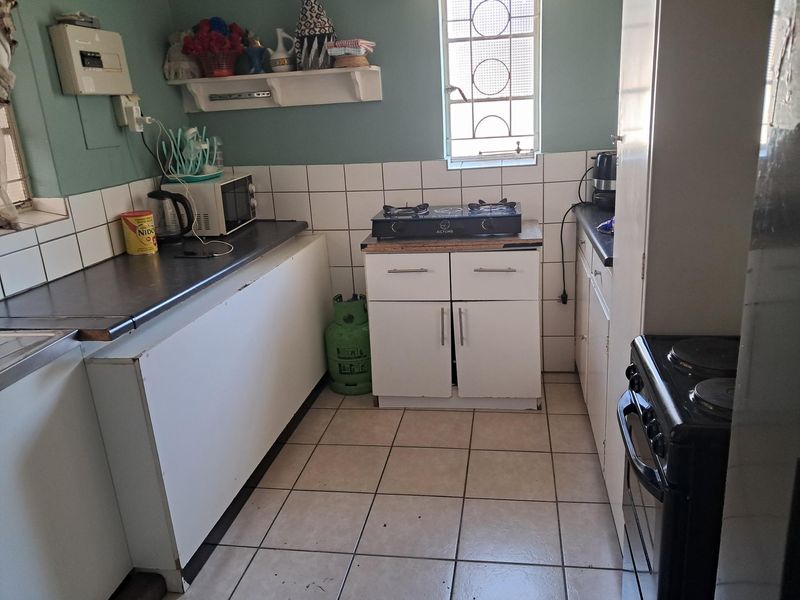A functional kitchen featuring tiled flooring, white cabinetry, laminate countertops, and a gas hob, with a security-grille window providing natural light.