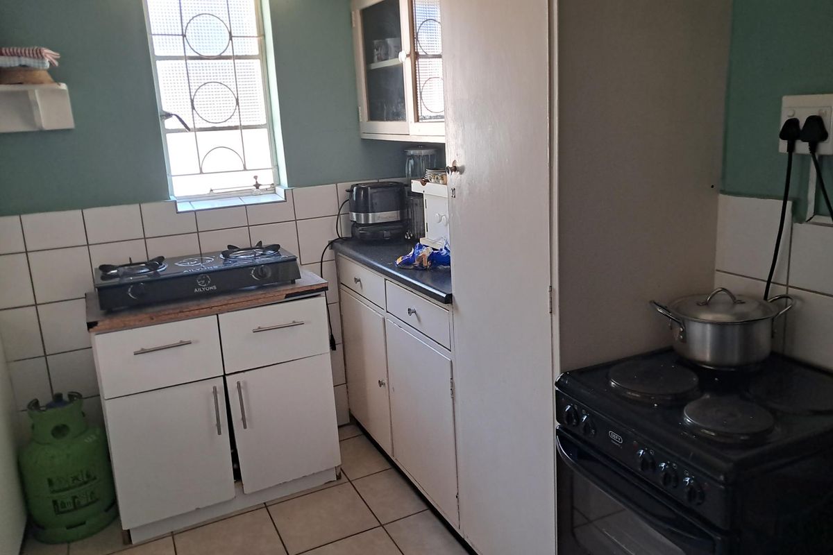 A compact kitchen featuring tiled flooring, a tiled backsplash, built-in cabinetry with laminate countertops, and an electric stove.
