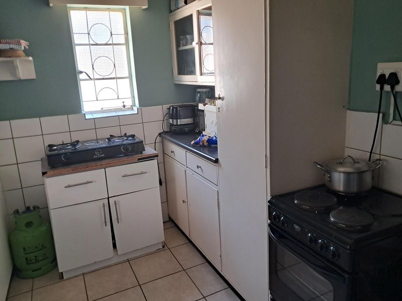 A compact kitchen featuring tiled flooring, a tiled backsplash, built-in cabinetry with laminate countertops, and an electric stove.
