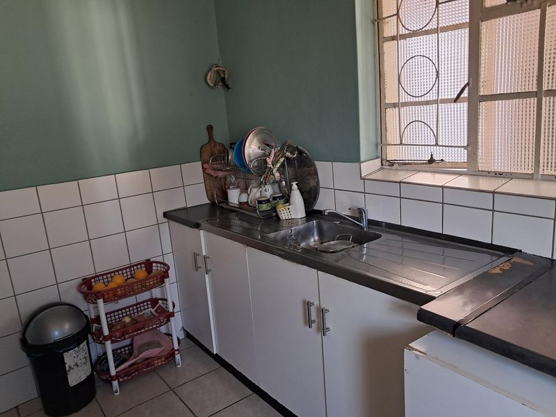 A compact kitchen area featuring a stainless steel sink, tiled backsplash, and built-in cabinetry with security bars on the window.