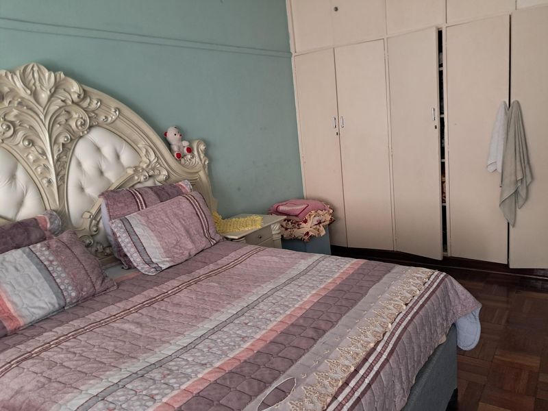 A bedroom featuring built-in cupboards and traditional parquet flooring, offering a functional space with potential for cosmetic updates.