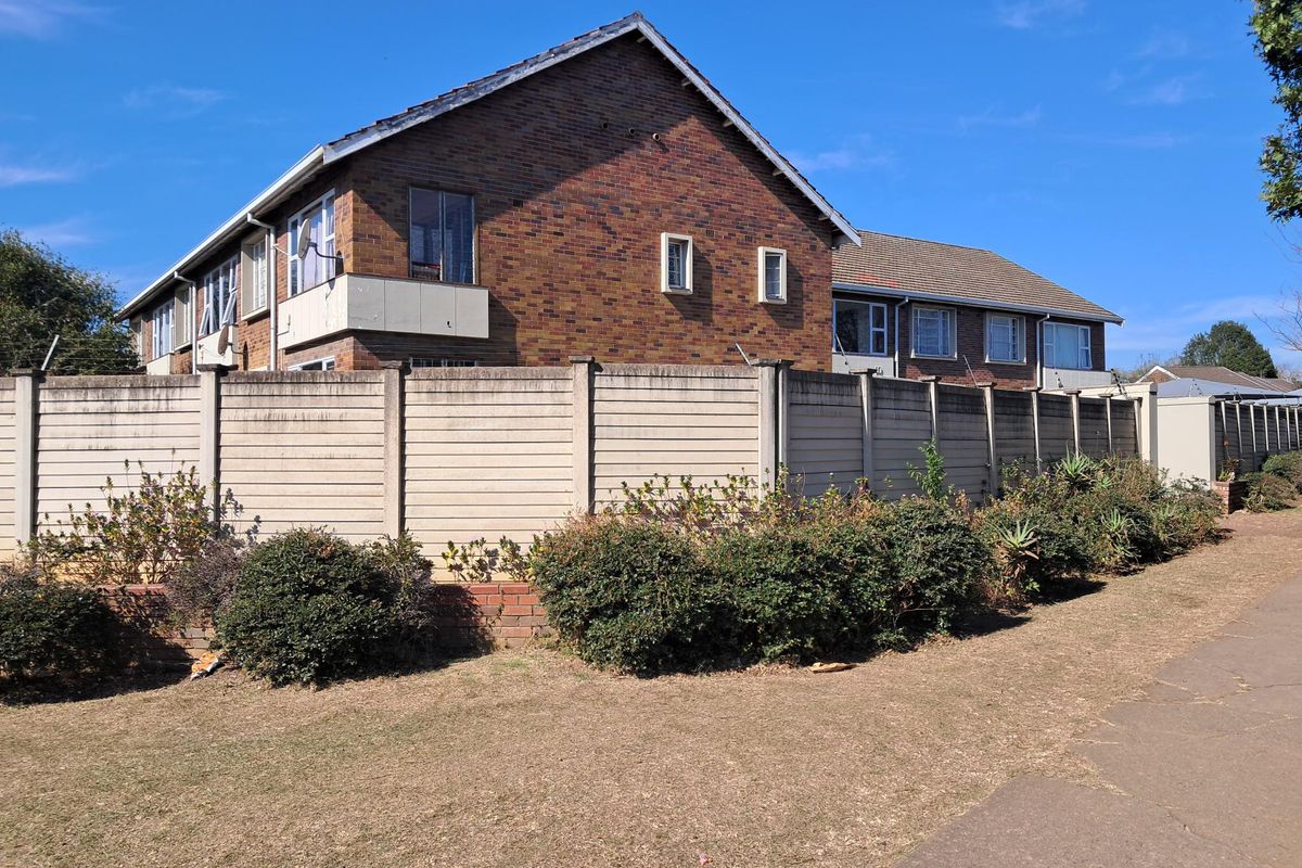 Exterior view of the apartment building featuring a brick facade, tiled roof, and a secure precast concrete boundary wall.