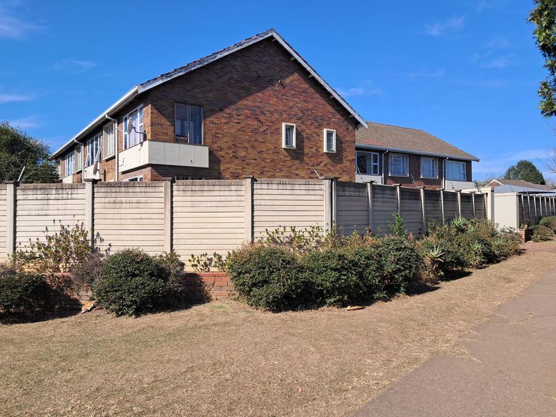 Exterior view of the apartment building featuring a brick facade, tiled roof, and a secure precast concrete boundary wall.