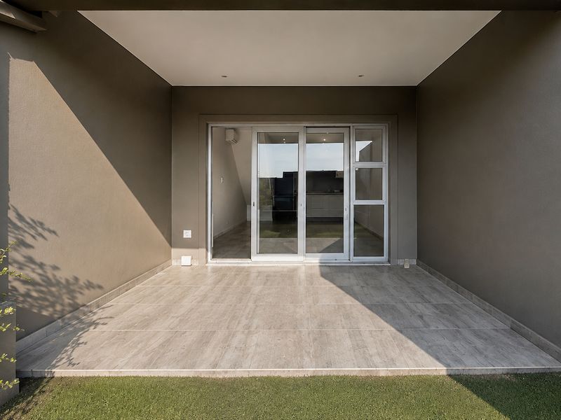 A modern covered patio featuring tiled flooring, stone cladding accents, and a large sliding glass door providing access to the interior living space.