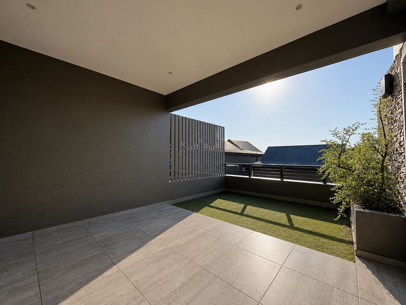 A modern, well-maintained covered balcony featuring tiled flooring, a section of artificial grass, stone cladding, and a slatted privacy screen.