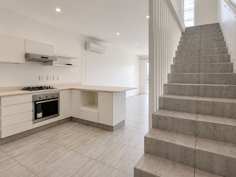 Modern open-plan kitchen and living area featuring sleek white cabinetry, integrated appliances, and a contemporary tiled staircase leading to the upper level.