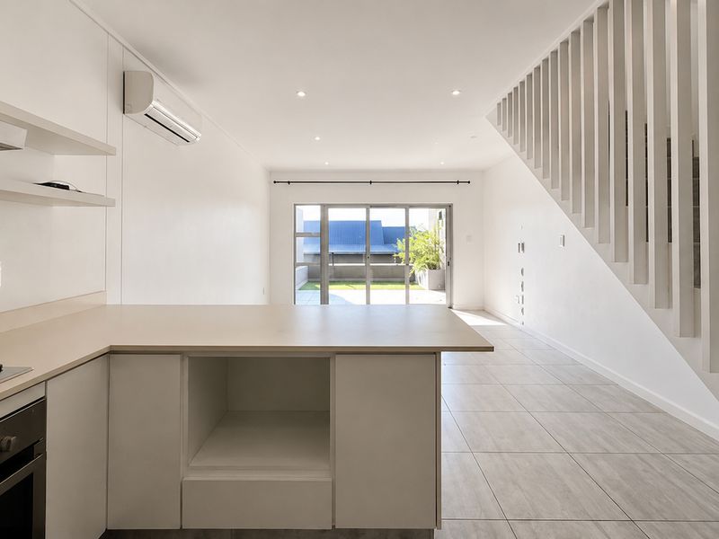 Bright open-plan living area featuring a modern kitchen with built-in appliances, tiled flooring, and a staircase, leading out to a patio area.
