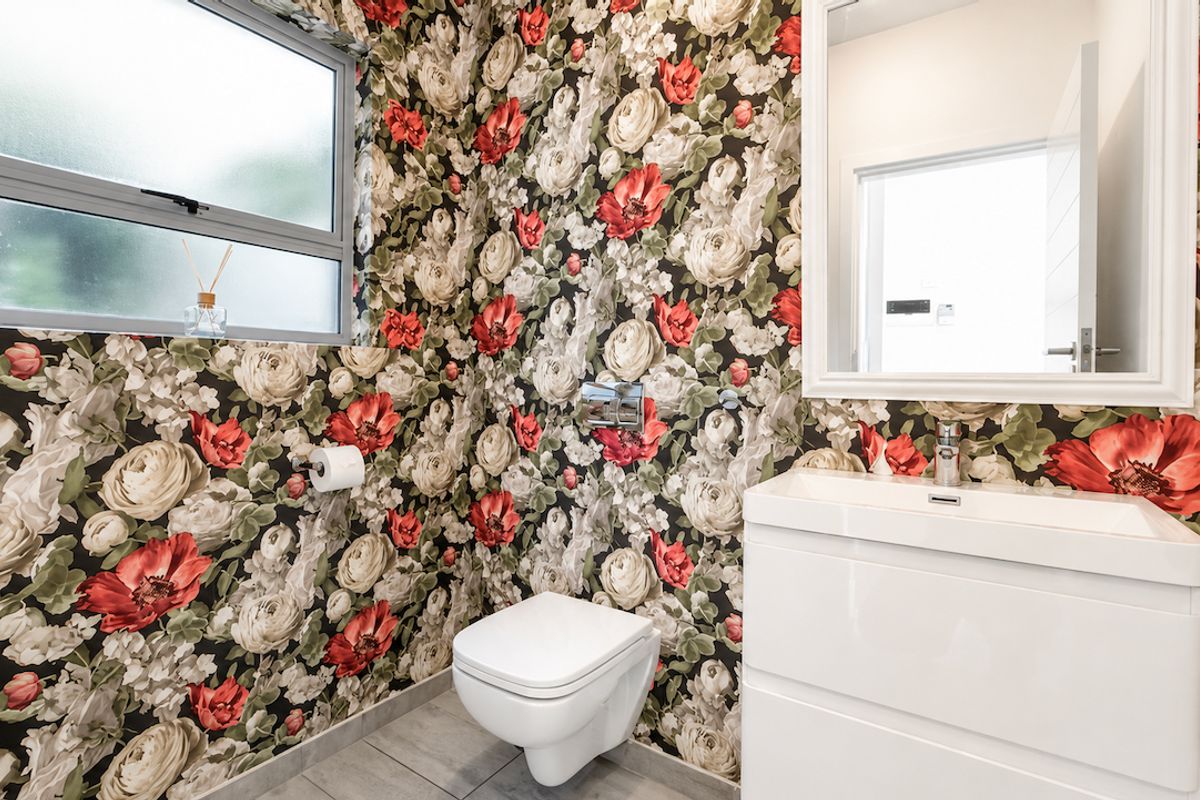 A modern bathroom featuring a wall-mounted toilet, white vanity with basin, and bold floral wallpaper, complemented by tiled flooring and a framed mirror.