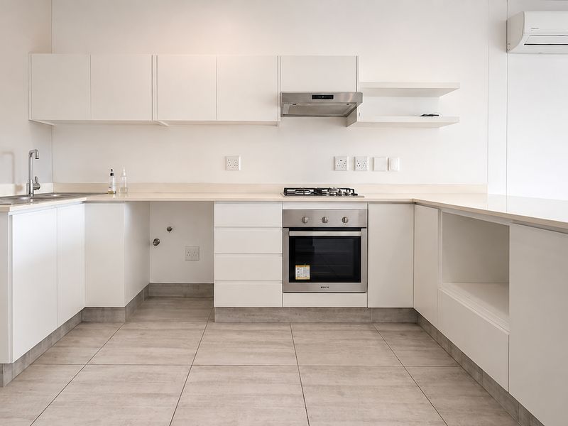 Modern, minimalist kitchen featuring white cabinetry, stone countertops, integrated stainless steel oven, gas hob, extractor fan, and tiled flooring.
