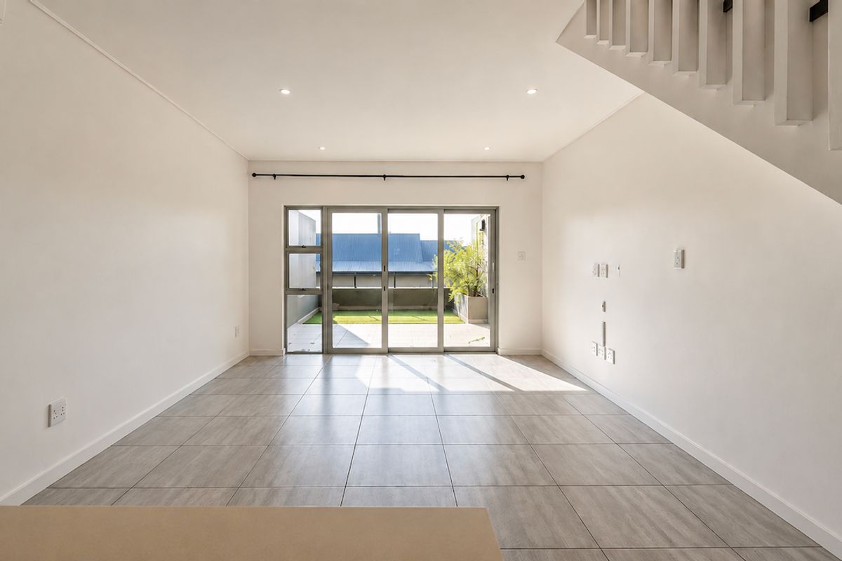 A bright, open-plan living area featuring neutral tiled flooring, recessed lighting, and large sliding glass doors that provide access to an outdoor space.
