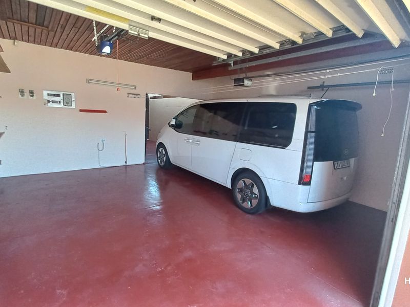 A functional double garage featuring a painted concrete floor, timber ceiling, and built-in storage shelving.