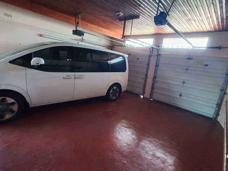A spacious double garage featuring a timber-lined ceiling, painted concrete flooring, and built-in storage shelving.
