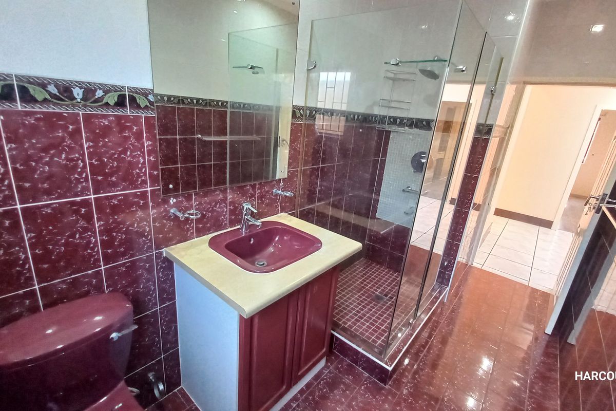A functional bathroom featuring a vanity with integrated sink, glass-enclosed shower, and floor-to-ceiling wall tiling.