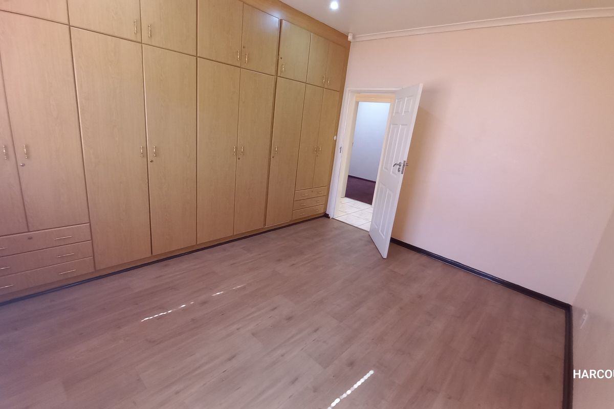 A clean, empty bedroom featuring extensive built-in wooden cupboards and modern laminate flooring, offering a neutral space ready for personalization.