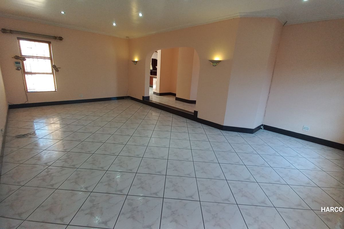 Spacious, empty living area featuring neutral tiled flooring, recessed lighting, and a decorative archway leading to an adjacent room.