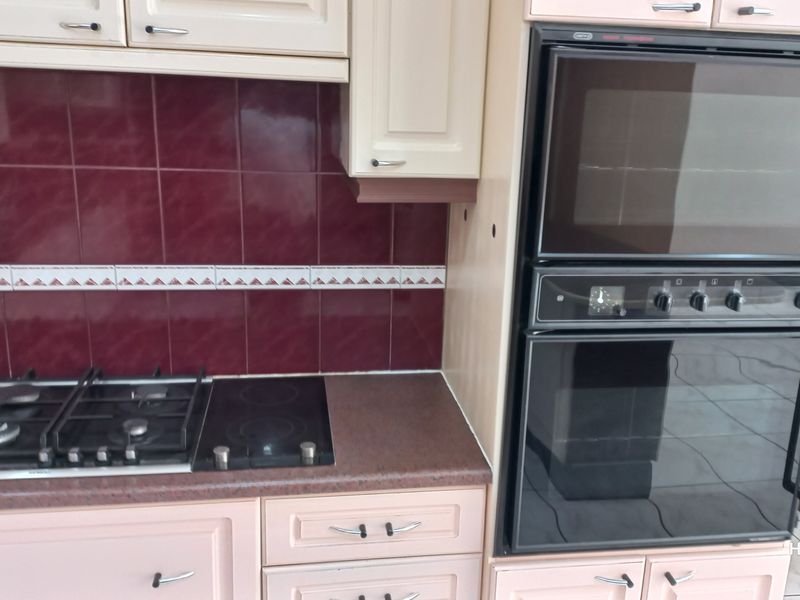 A kitchen area featuring a combination gas and electric hob, tiled backsplash, and a built-in double oven unit with fitted cabinetry.