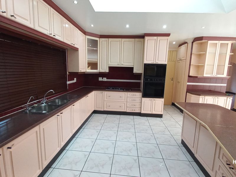 Spacious kitchen featuring extensive built-in cabinetry, a central island, double sink, and integrated oven and hob, offering a functional layout for culinary activities.