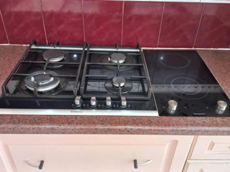 A kitchen workspace featuring a combined Siemens gas and electric hob set into a granite countertop with a tiled backsplash.