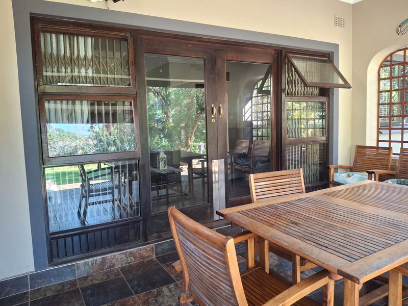 A covered patio area featuring dark timber-framed glass doors, security screens, and durable tiled flooring, providing a seamless transition to the outdoor space.