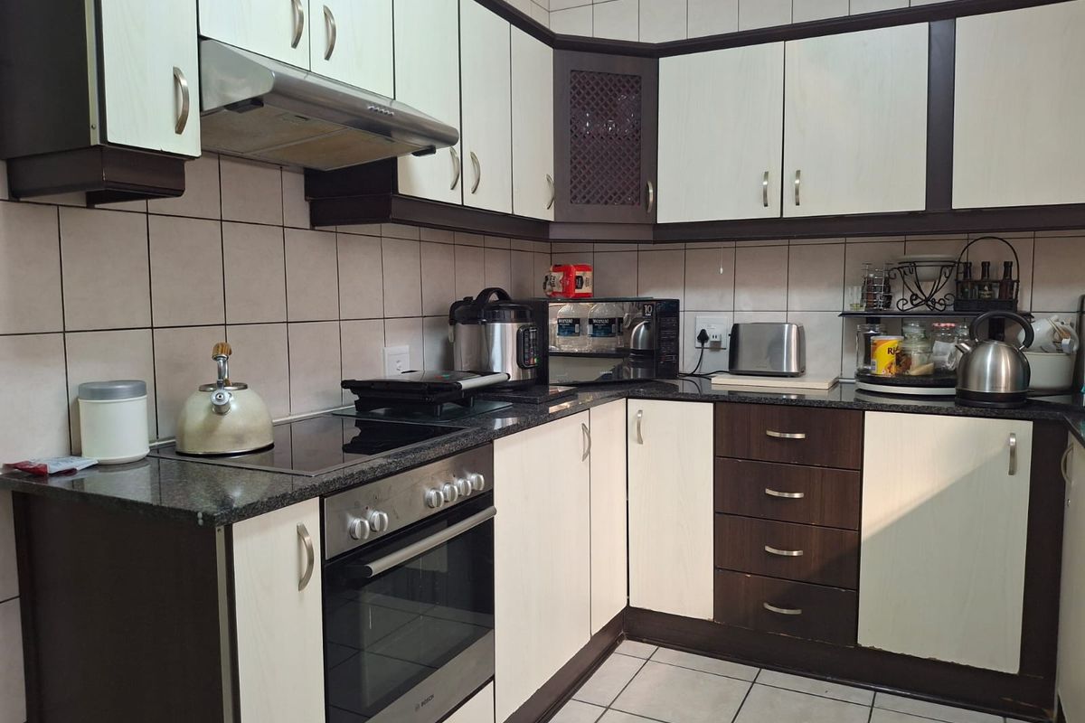 A functional kitchen featuring built-in cabinetry, granite countertops, a tiled backsplash, and integrated appliances including an oven and extractor fan.