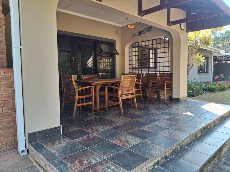 A covered patio area featuring dark tiled flooring, arched masonry pillars, and a timber roof structure, providing a functional outdoor entertainment space.