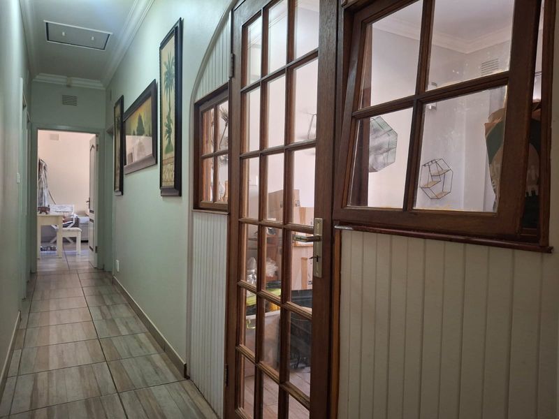 A well-lit hallway featuring tiled flooring, beadboard wall paneling, and timber-framed glass doors leading into an adjacent room.