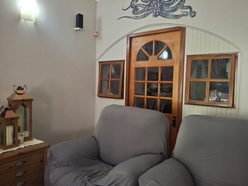 A living room area featuring a distinctive arched timber-framed glass door flanked by matching timber-framed windows and wall-mounted lighting.