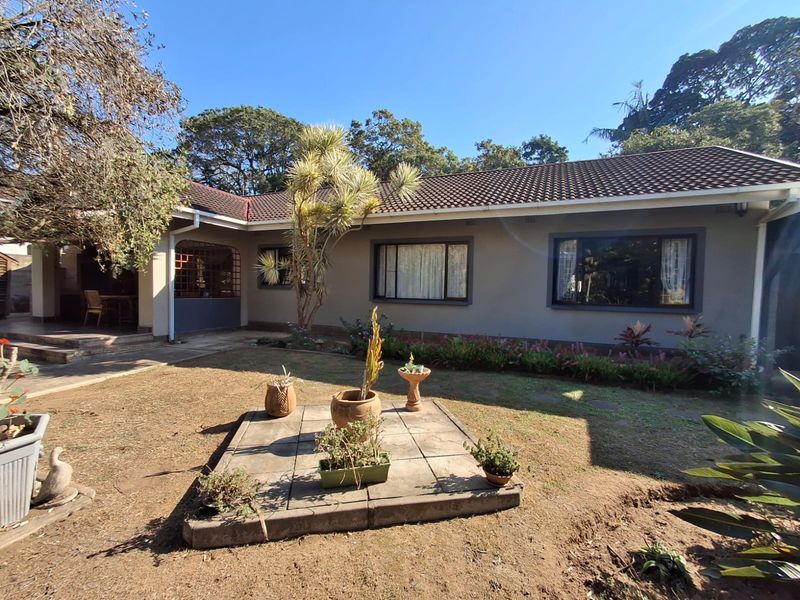 Rear view of the house featuring a tiled roof, concrete patio area, and a landscaped garden with a central paved feature.