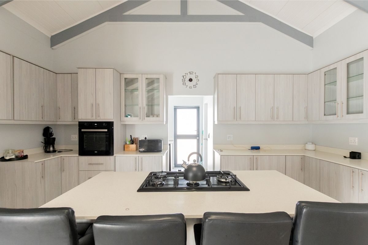 Modern kitchen featuring light wood cabinetry, stone countertops, a central island with a gas hob, and a high vaulted ceiling.