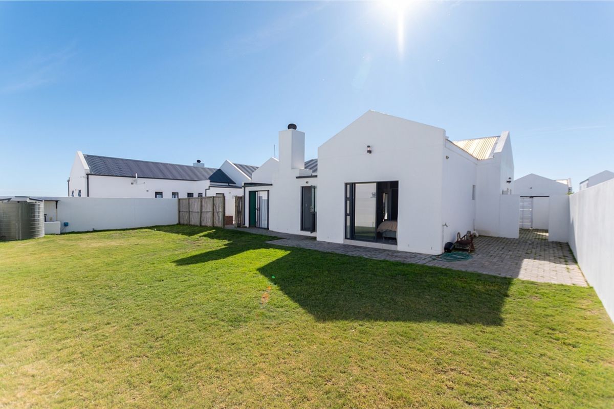 Rear view of the property featuring a paved patio area, a well-maintained lawn, and a white exterior finish with a prominent chimney.