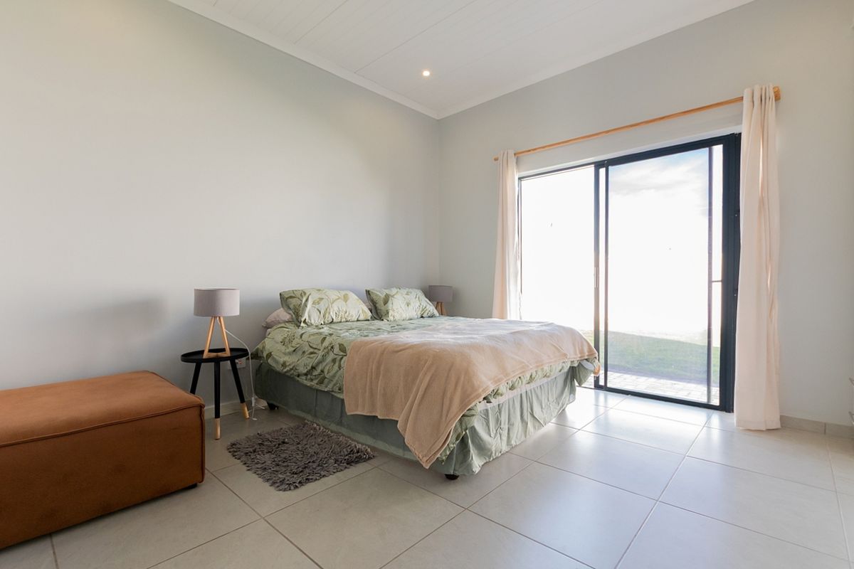 A bright bedroom featuring large sliding glass doors that provide natural light and direct access to the outdoor area, complemented by neutral tiled flooring.