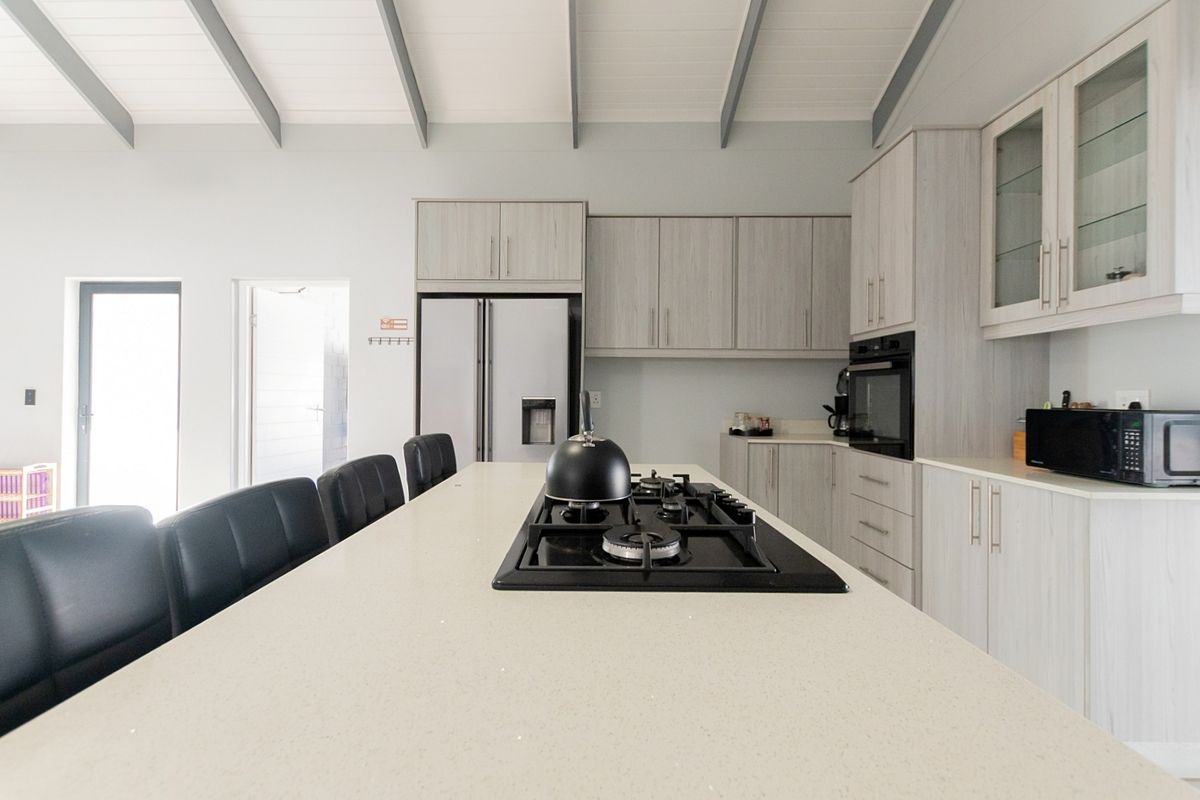 Modern kitchen featuring a central island with a built-in gas cooktop, light wood-grain cabinetry, and a high vaulted ceiling with exposed beams.