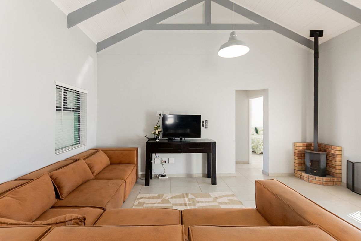 Spacious living room featuring a high vaulted ceiling with exposed rafters, tiled flooring, and a cozy wood-burning fireplace with a brick hearth.