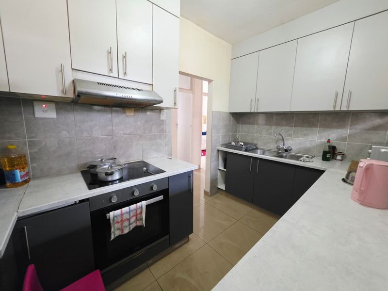 A functional kitchen featuring modern two-tone cabinetry, a built-in oven with electric hob, extractor fan, and a double sink with tiled splashback.