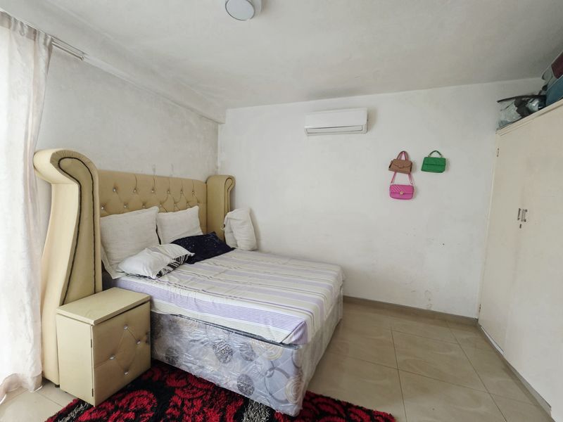 A bedroom featuring tiled flooring, a built-in wardrobe, and a wall-mounted split-system air conditioner. The room requires cosmetic wall repairs and fresh paint.