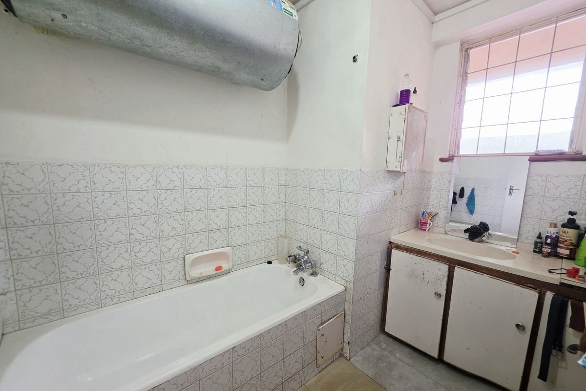 A dated bathroom featuring a standard bathtub, vanity basin, and wall-mounted water heater, requiring cosmetic updates to modernize the space.