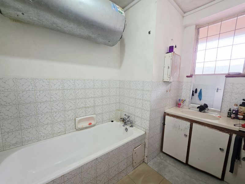 A dated bathroom featuring a standard bathtub, vanity basin, and wall-mounted water heater, requiring cosmetic updates to modernize the space.