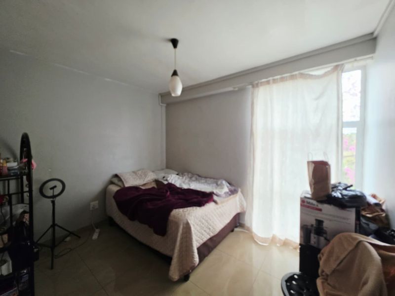 A simple bedroom featuring tiled flooring and a central pendant light fixture, offering a functional space with neutral wall finishes.